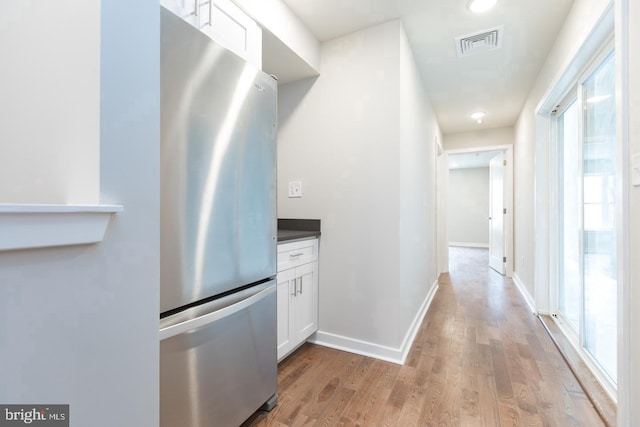 kitchen with stainless steel fridge, white cabinets, light wood-type flooring, and plenty of natural light