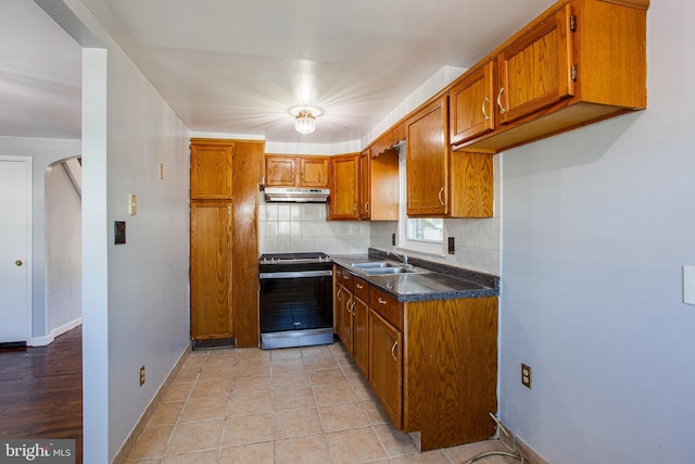 kitchen with stainless steel range oven, backsplash, sink, and light tile floors