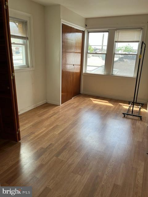 unfurnished bedroom with wood-type flooring, a closet, and multiple windows