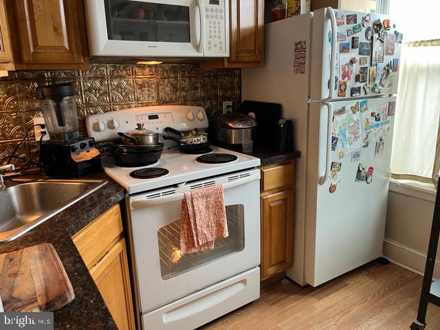 kitchen featuring light wood-type flooring, decorative backsplash, white appliances, and sink