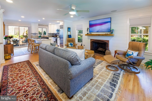 living room with light hardwood / wood-style flooring, ornamental molding, ceiling fan, and a fireplace