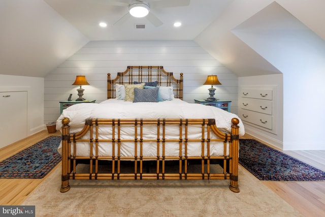 bedroom with wood walls, lofted ceiling, ceiling fan, and light wood-type flooring