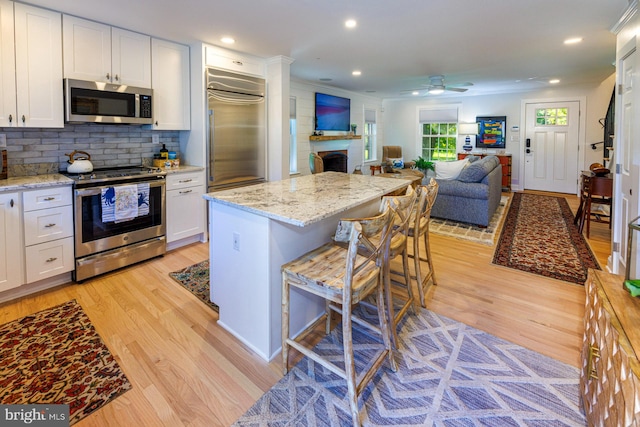 kitchen featuring white cabinetry, ceiling fan, a kitchen bar, light hardwood / wood-style flooring, and stainless steel appliances