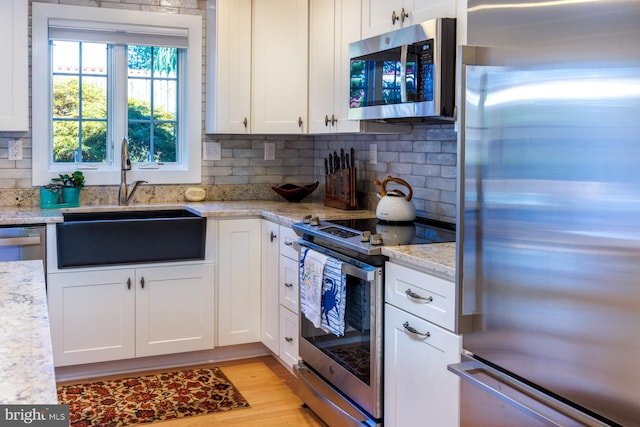 kitchen with white cabinets, light stone countertops, light hardwood / wood-style floors, and appliances with stainless steel finishes