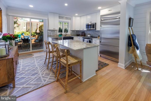 kitchen featuring light stone counters, stainless steel appliances, backsplash, light hardwood / wood-style floors, and white cabinets