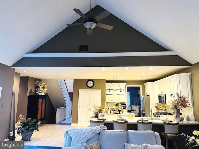 kitchen with white cabinetry, a kitchen bar, stainless steel appliances, pendant lighting, and ceiling fan with notable chandelier