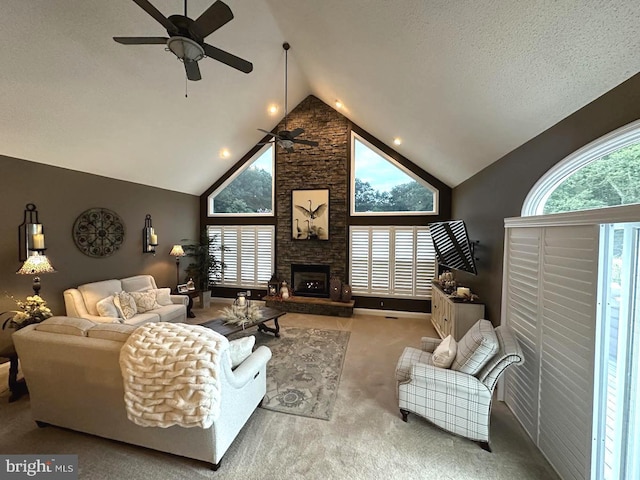 living room with ceiling fan, carpet, high vaulted ceiling, a textured ceiling, and a stone fireplace