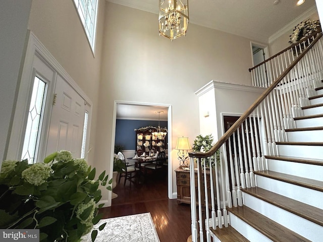 stairs with a notable chandelier, crown molding, dark wood-type flooring, and a towering ceiling