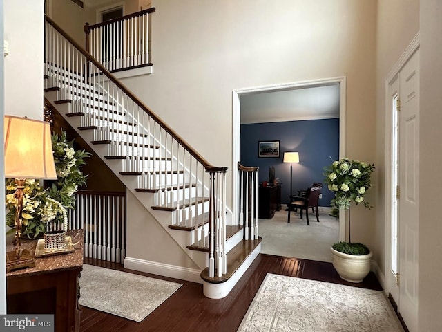 stairway with ornamental molding, dark colored carpet, and a towering ceiling