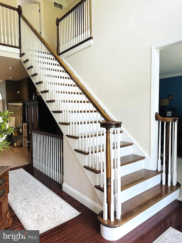 stairs with crown molding, dark wood-type flooring, and a high ceiling