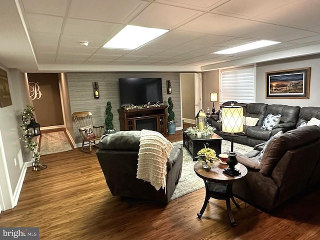 living room with a fireplace, dark wood-type flooring, and a drop ceiling