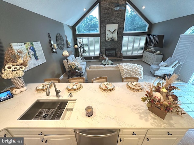 kitchen with high vaulted ceiling, brick wall, a large fireplace, white cabinetry, and light stone counters