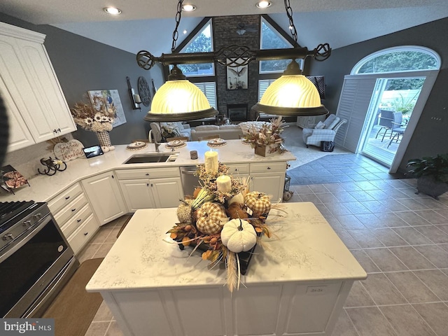 kitchen with appliances with stainless steel finishes, a brick fireplace, light tile floors, sink, and white cabinets