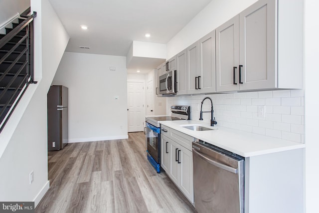 kitchen with light wood-type flooring, stainless steel appliances, sink, and tasteful backsplash