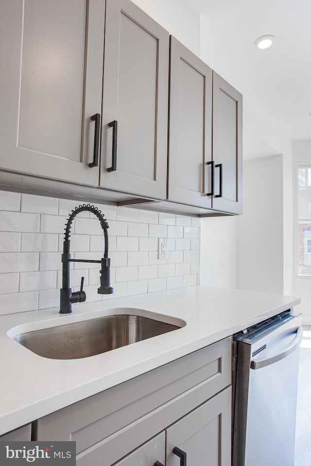 kitchen with stainless steel dishwasher, gray cabinetry, sink, and decorative backsplash