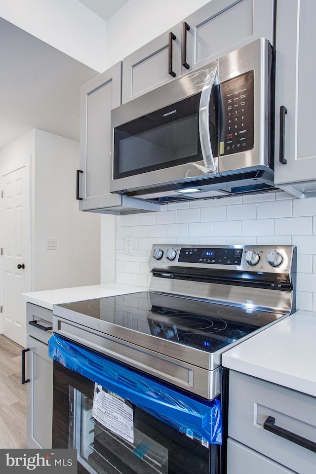 interior space featuring gray cabinets, tasteful backsplash, light hardwood / wood-style flooring, and stainless steel appliances