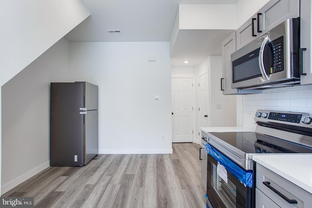 kitchen featuring stainless steel appliances, light hardwood / wood-style floors, decorative backsplash, and gray cabinets