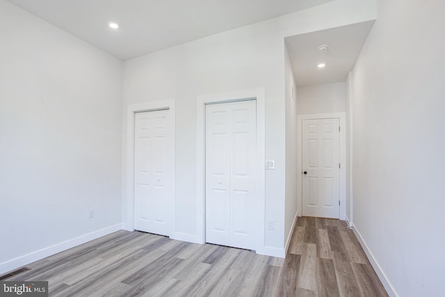 unfurnished bedroom with light hardwood / wood-style floors and multiple closets