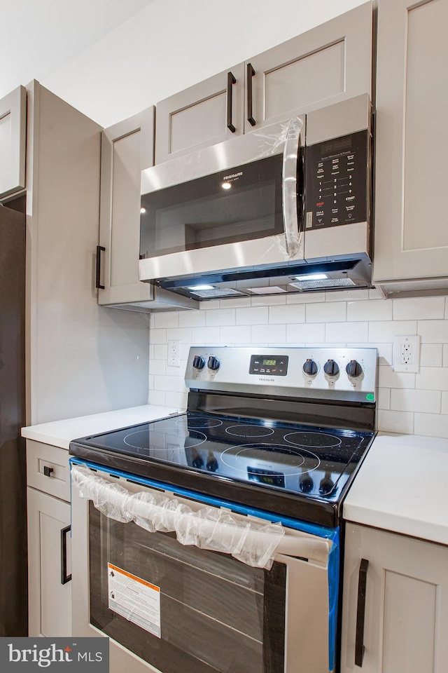 kitchen with gray cabinets, backsplash, and appliances with stainless steel finishes