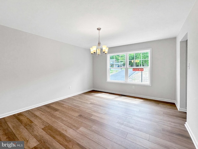 spare room with a chandelier and light wood-type flooring