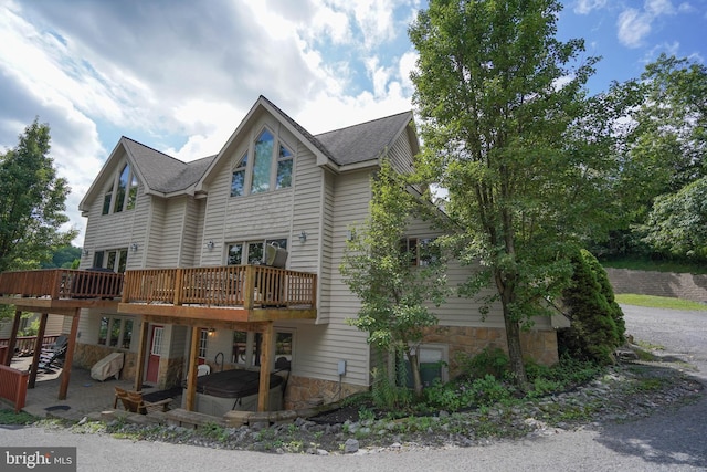 exterior space featuring a deck, a patio, roof with shingles, and a jacuzzi