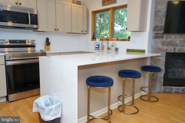 kitchen featuring light hardwood / wood-style flooring, a breakfast bar, appliances with stainless steel finishes, sink, and a fireplace