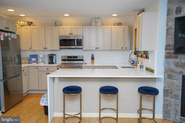 kitchen featuring a kitchen breakfast bar, appliances with stainless steel finishes, light hardwood / wood-style floors, sink, and kitchen peninsula