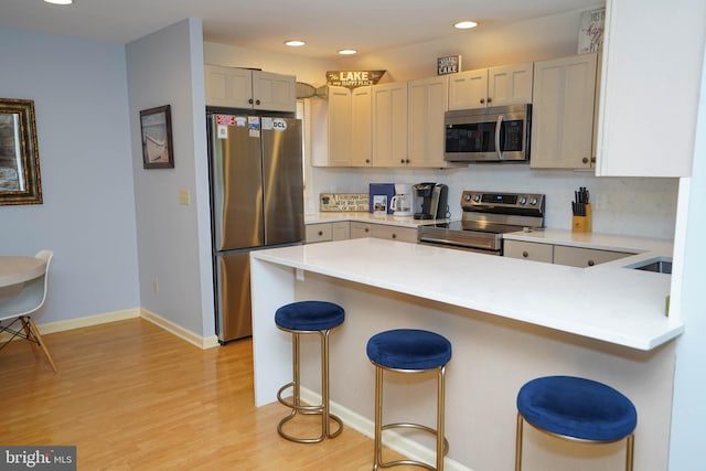 kitchen featuring light countertops, appliances with stainless steel finishes, light wood-style floors, a peninsula, and a kitchen bar