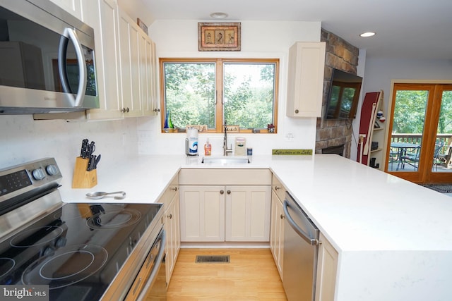 kitchen with appliances with stainless steel finishes, backsplash, sink, light wood-type flooring, and kitchen peninsula