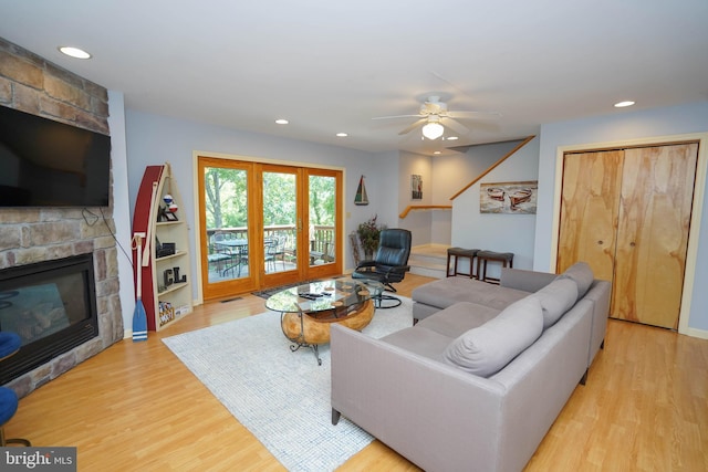 living room with ceiling fan, light hardwood / wood-style flooring, and a stone fireplace