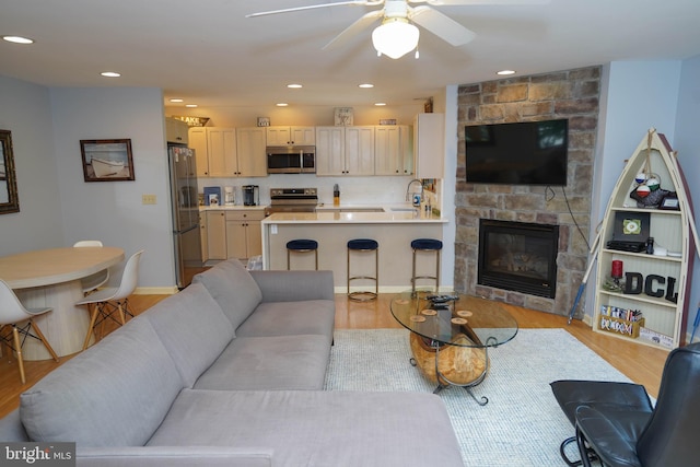 living room with ceiling fan, a fireplace, light hardwood / wood-style flooring, and sink