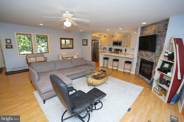 living room with ceiling fan, a stone fireplace, and light wood-type flooring