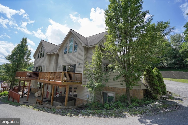 exterior space with stone siding, a patio area, a wooden deck, and roof with shingles