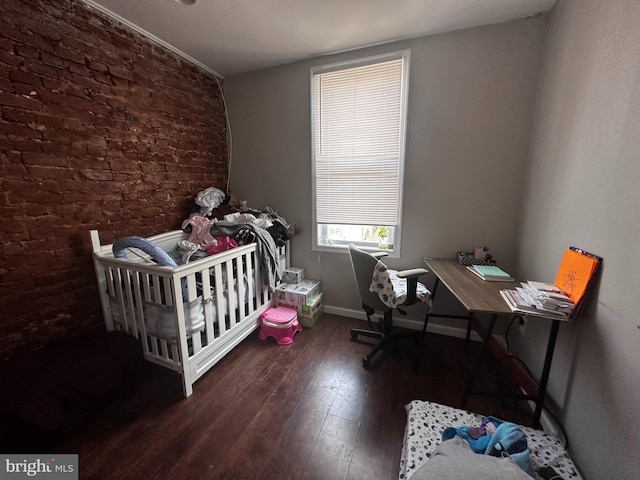 bedroom with brick wall, dark wood-type flooring, and a crib