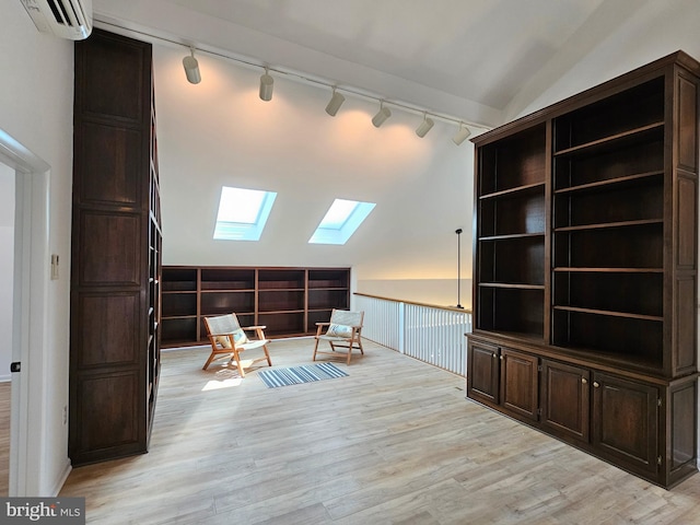 interior space featuring an AC wall unit, lofted ceiling with skylight, and light hardwood / wood-style floors