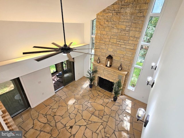 living room with dark tile floors, ceiling fan, high vaulted ceiling, and a stone fireplace