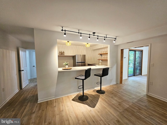 kitchen featuring kitchen peninsula, stainless steel fridge, a kitchen breakfast bar, rail lighting, and dark wood-type flooring