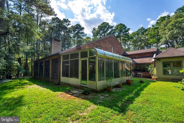 rear view of house with central AC unit, a yard, and a sunroom