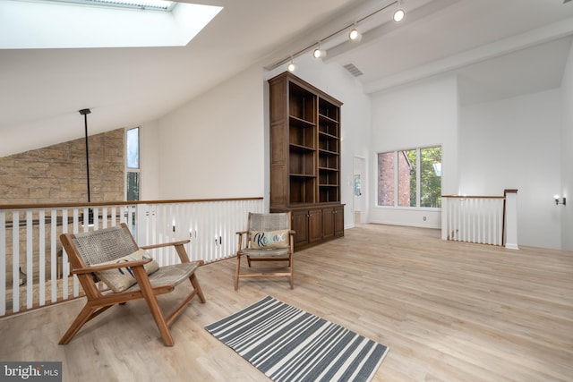 sitting room with light hardwood / wood-style floors, vaulted ceiling with skylight, and track lighting