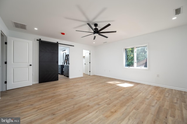 unfurnished bedroom with light hardwood / wood-style flooring and a barn door