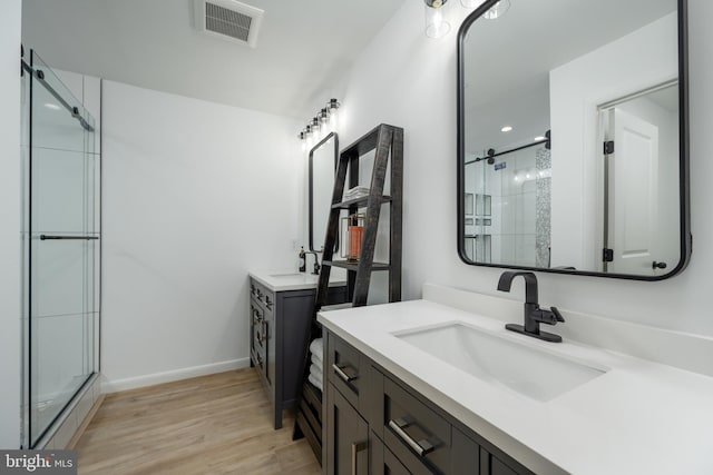 bathroom featuring dual bowl vanity, walk in shower, and wood-type flooring