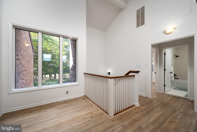 empty room with light hardwood / wood-style flooring, beam ceiling, a wealth of natural light, and high vaulted ceiling