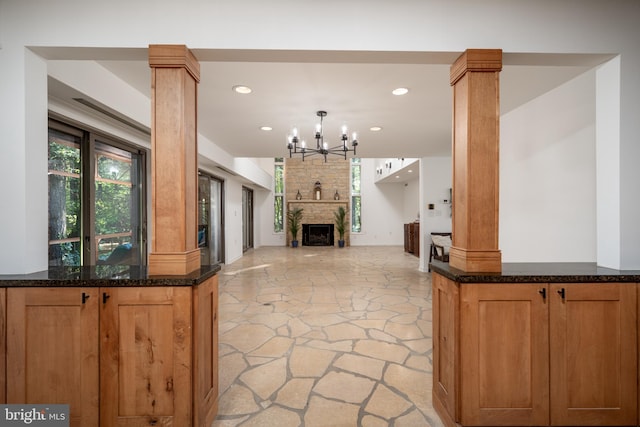 kitchen with a fireplace, dark stone countertops, decorative light fixtures, a chandelier, and ornate columns