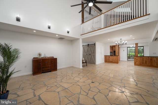 unfurnished living room featuring a barn door, ceiling fan, and a towering ceiling