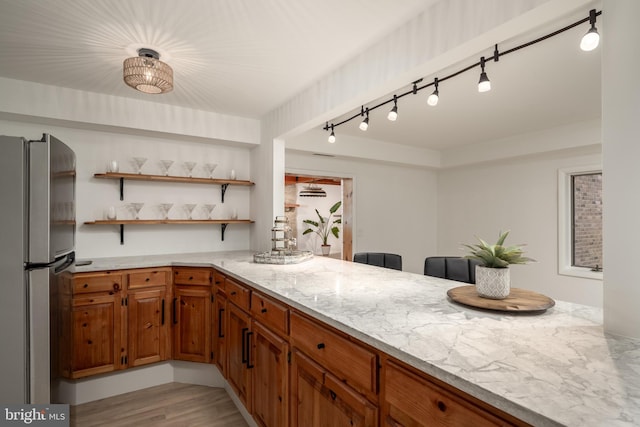 kitchen with stainless steel refrigerator, track lighting, light stone countertops, and light hardwood / wood-style flooring