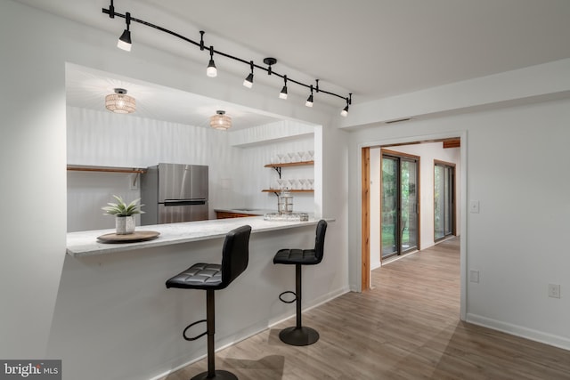 kitchen featuring kitchen peninsula, stainless steel fridge, a breakfast bar, track lighting, and wood-type flooring