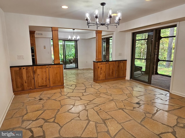 unfurnished room featuring decorative columns, a chandelier, and a healthy amount of sunlight