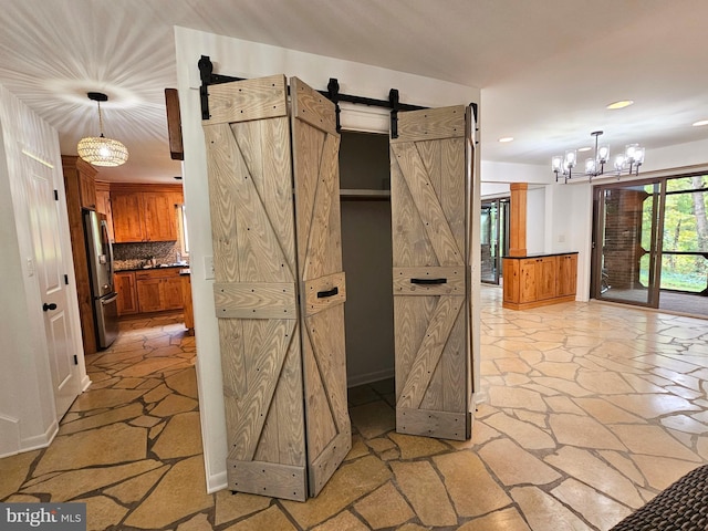 kitchen with a notable chandelier, a barn door, stainless steel fridge, backsplash, and hanging light fixtures