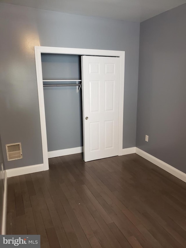 unfurnished bedroom with dark wood-type flooring and a closet