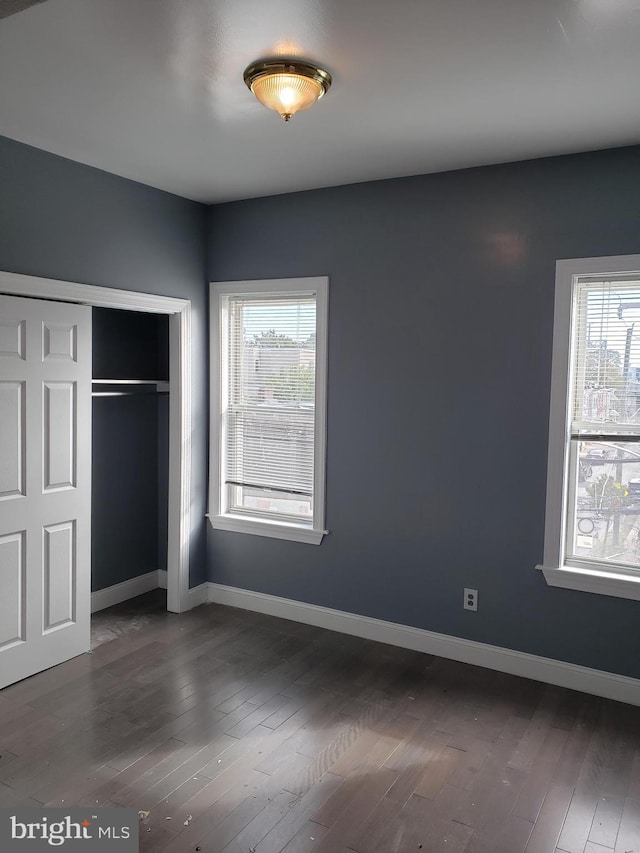 unfurnished bedroom with a closet, multiple windows, and dark hardwood / wood-style flooring